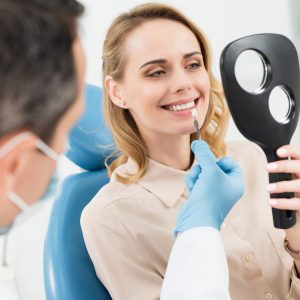 Female patient choosing tooth implant looking at mirror in modern dental clinic